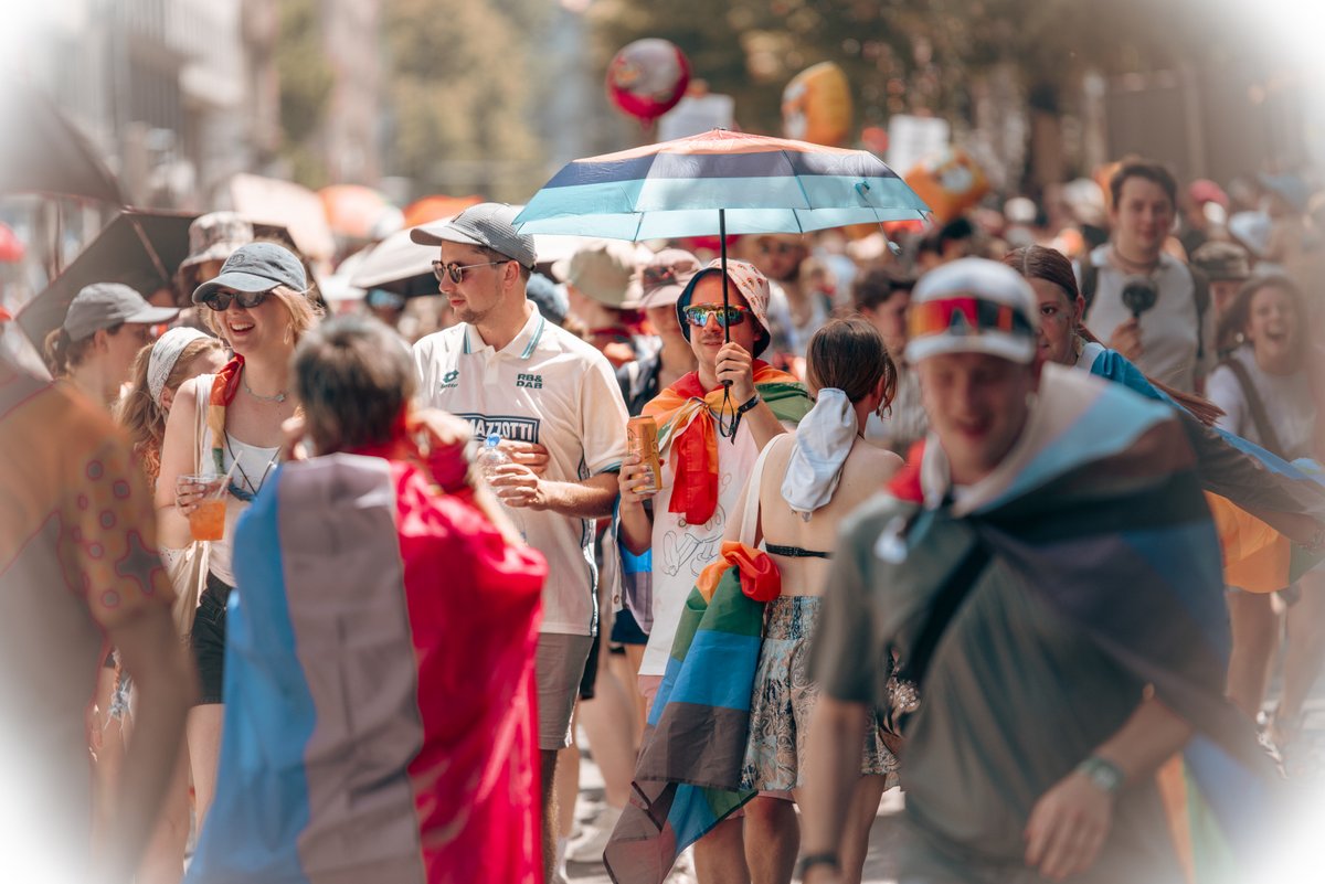 Viele Teilnehmende mit Pride-Flaggen und Sonnenschirmen genie?n den CSD München Pride 2026 bei hochsommerlichen Temperaturen.