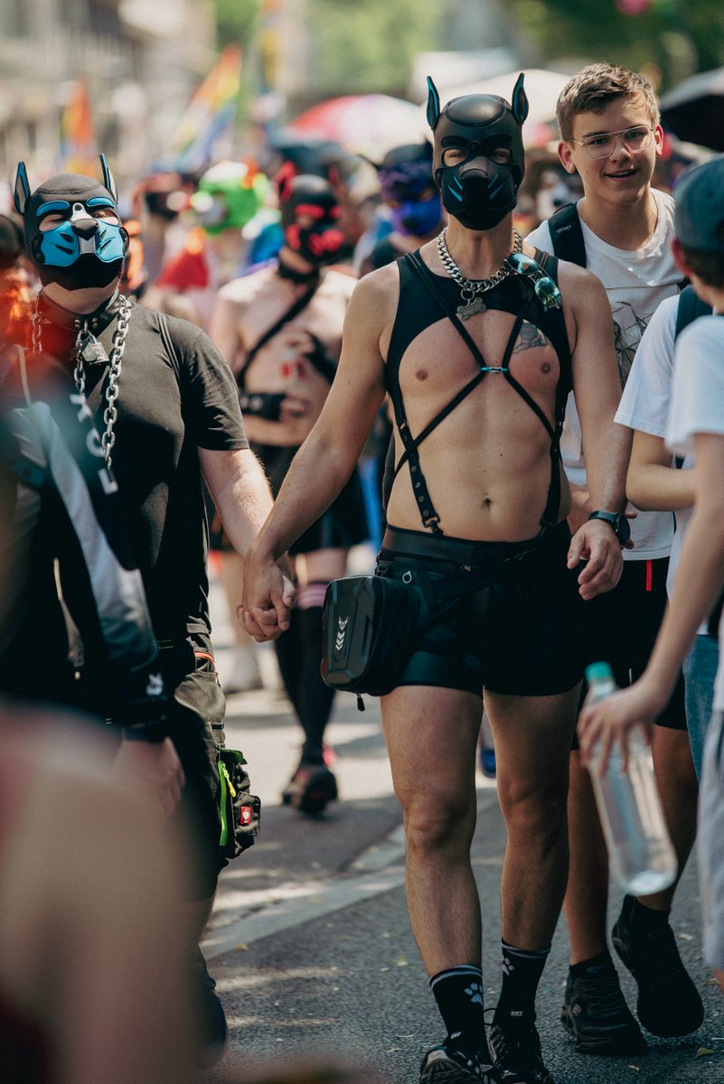 Person in schwarzem Lederlook und Maske geht neben anderen Teilnehmenden in der Parade.