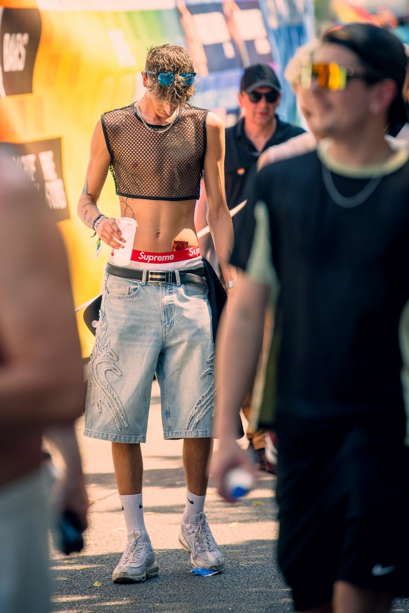 Teilnehmer in sommerlichem Outfit und Sonnenbrille steht vor einem Pride-Wagen in der Parade.
