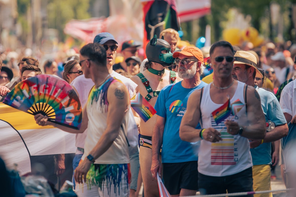 Bunte Gruppe von Teilnehmenden zieht durch die Menge, einige tragen Regenbogenaccessoires.