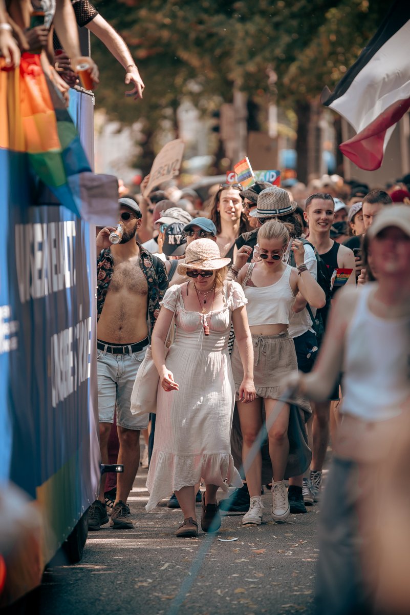 Gruppe wei?gekleideter Teilnehmender zieht neben einem Paradewagen durch die Stra?.