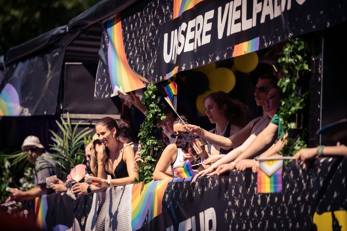 Teilnehmende stehen auf einem Wagen unter einem Banner mit der Botschaft ?Unsere Vielfalt, unsere St?ke?.