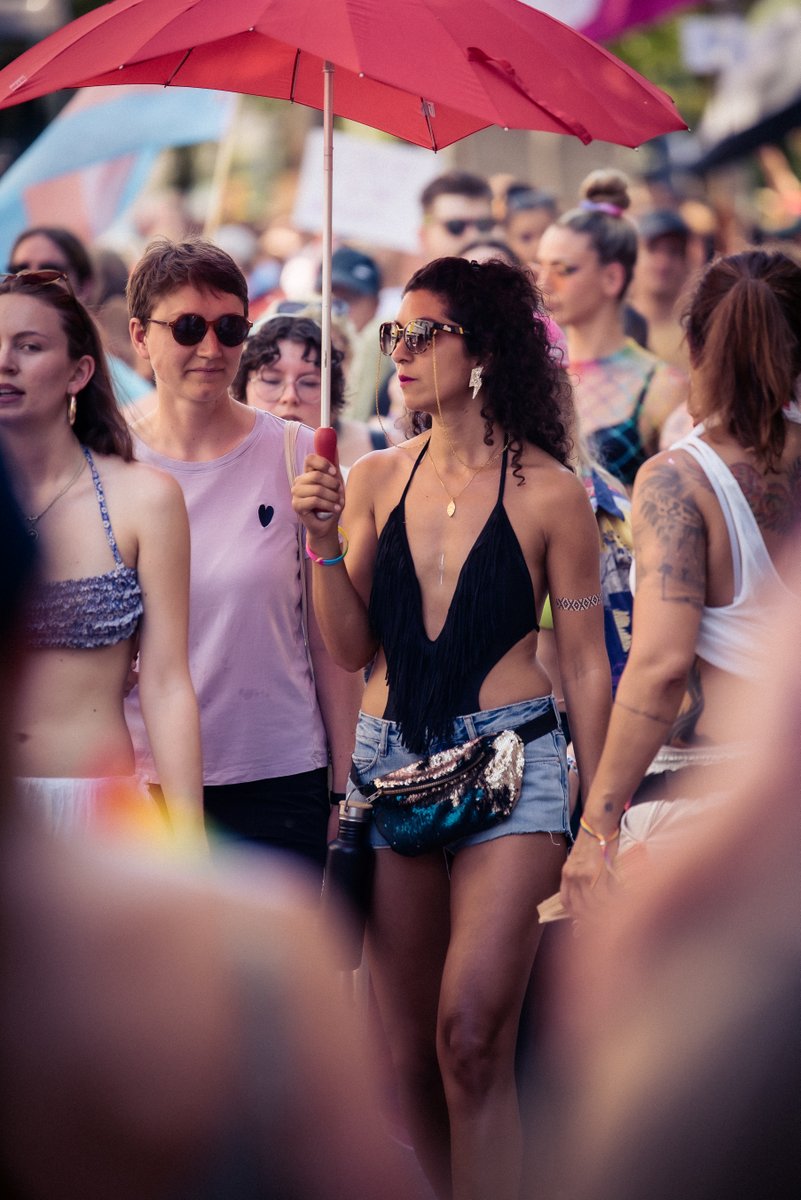 Gruppe junger Menschen l?ft mit Getr?ken und Pride-Accessoires durch die sonnige Stra?.