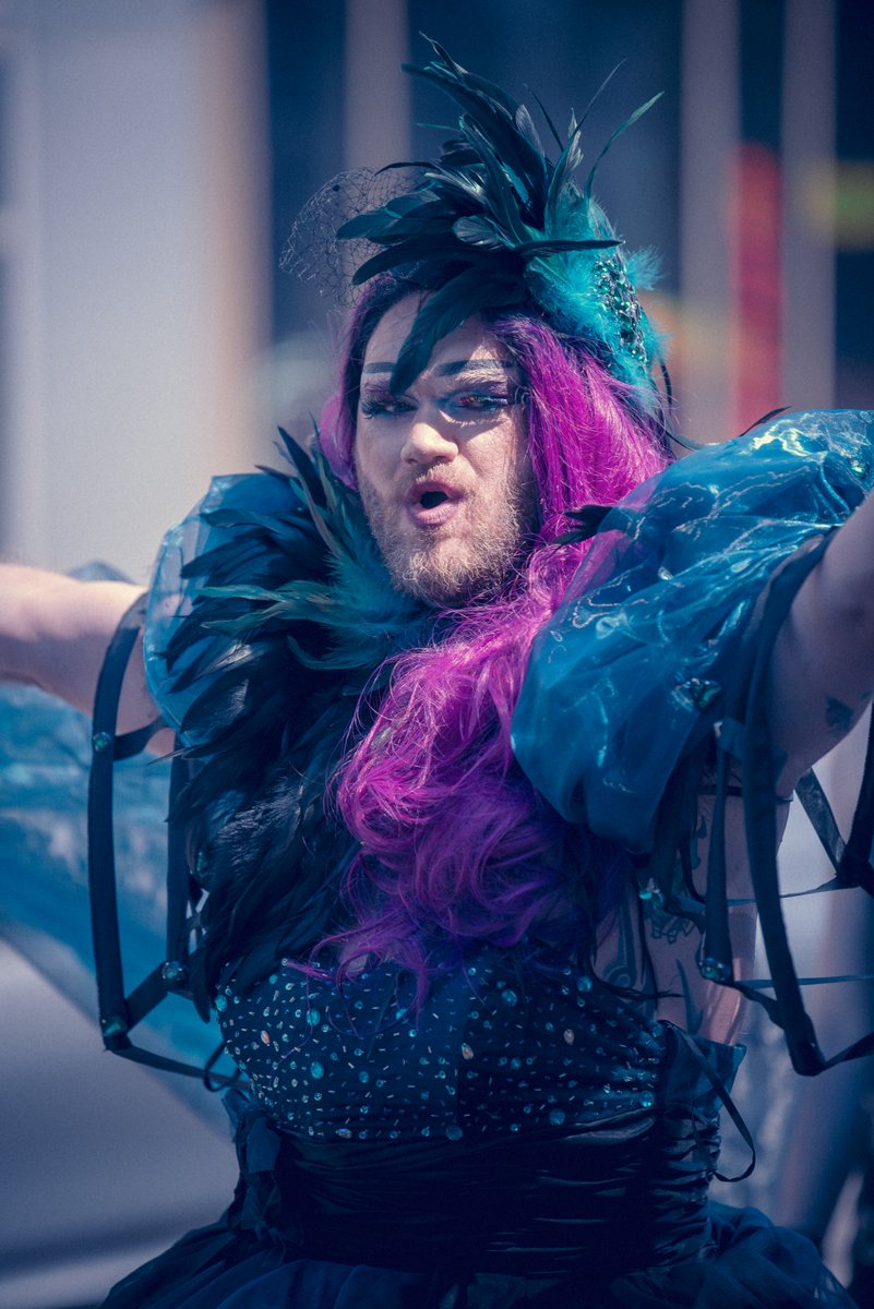 Drag Artist mit schwarzem Federkost? und pinken Haaren posiert im B?nenlicht.