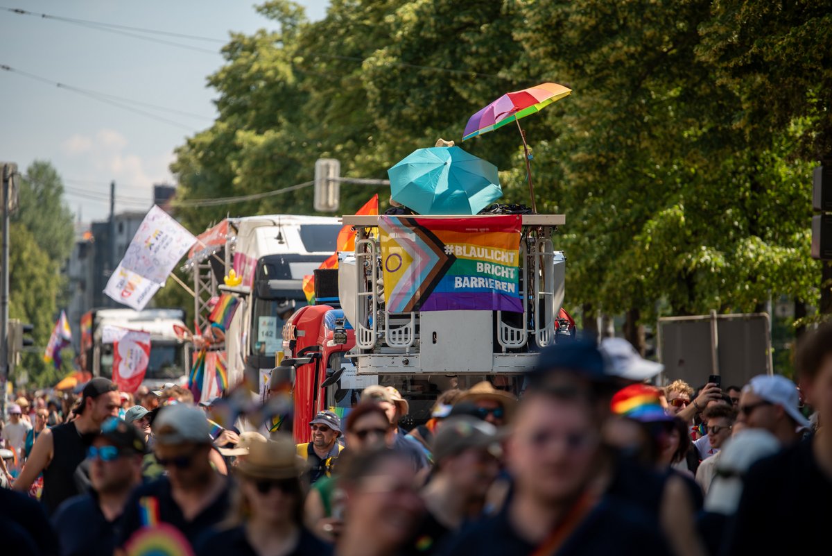 Paradezug mit Wagen und Regenbogenflaggen zieht durch die Menge auf der Stra?.