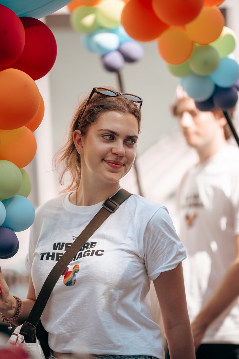 L?helnde Teilnehmerin im wei?n T-Shirt steht vor einem geschm?kten Wagen mit bunten Ballons.