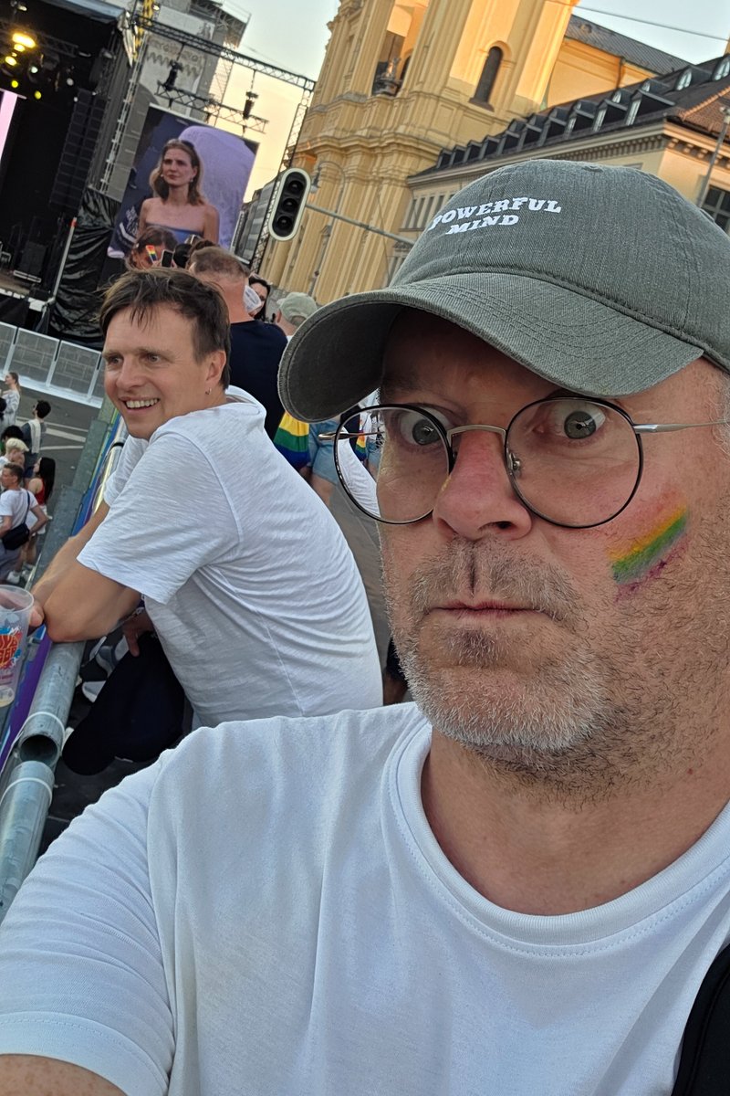 Selfie eines Besuchers mit Pride-Bemalung im Gesicht vor der Menschenmenge am Abend.