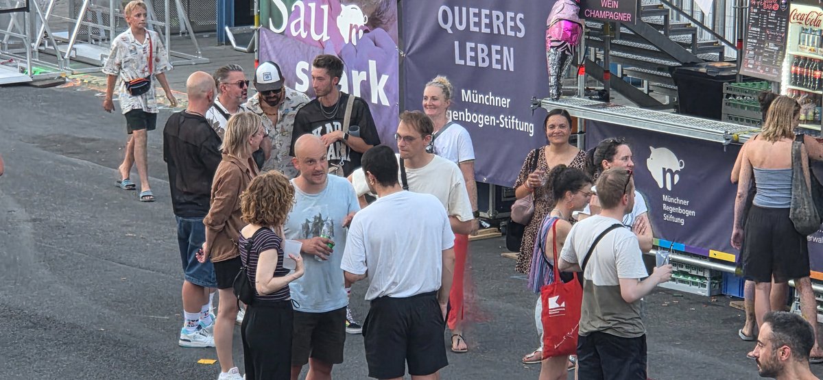 Gruppe von Besucherinnen und Besuchern steht vor einem Partybereich mit Schildern.