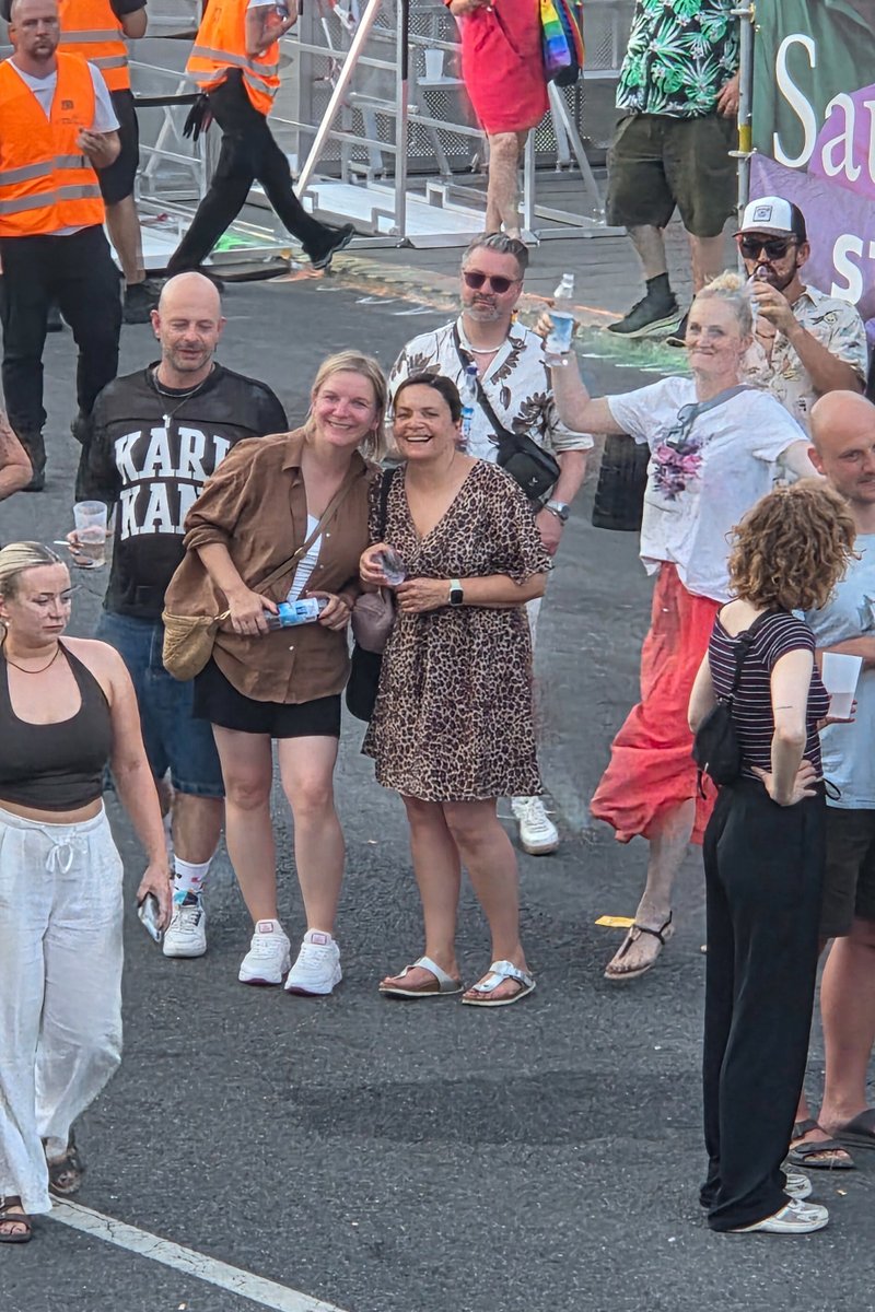 Kleine Gruppe posiert gemeinsam vor einer Absperrung beim abendlichen Pride-Fest.